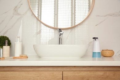 Modern automatic soap dispenser and other toiletries on countertop in bathroom