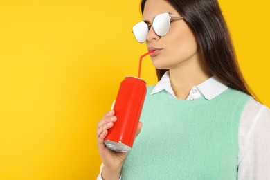Beautiful woman drinking from red beverage can on yellow background. Space for text