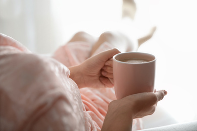 Photo of Woman with cup of hot drink at home in morning, closeup