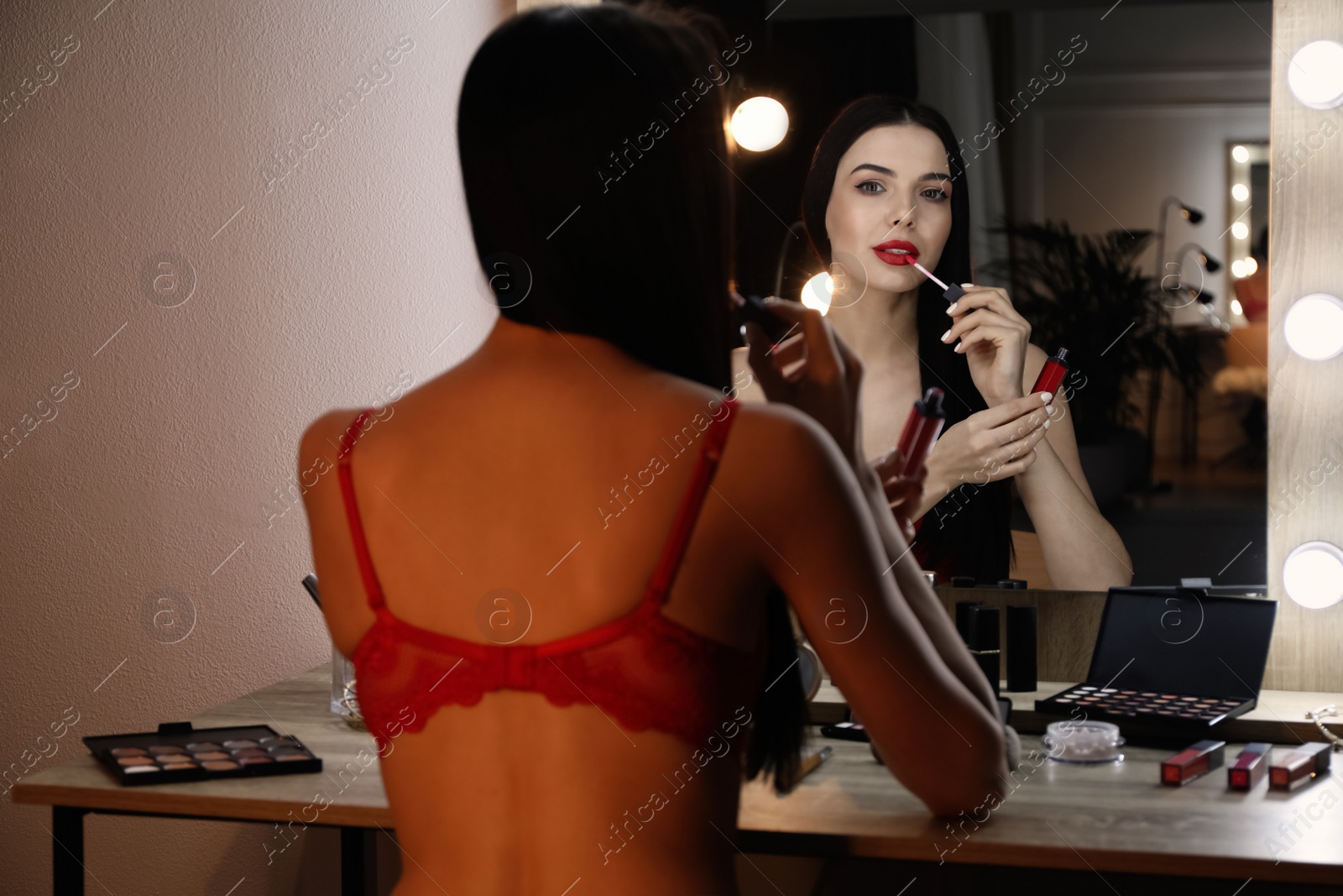 Photo of Beautiful woman applying makeup near mirror in room