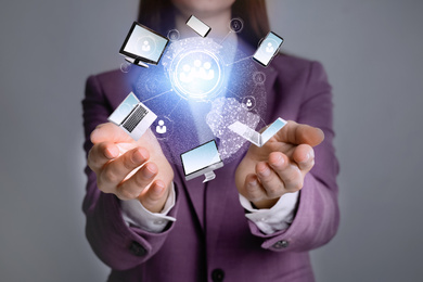 Image of Young businesswoman holding digital image of Earth and different devices in hands on grey background, closeup 