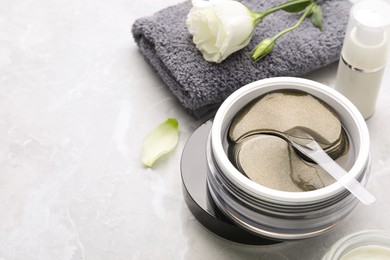 Photo of Package of under eye patches and flower on light grey marble table, space for text. Cosmetic product