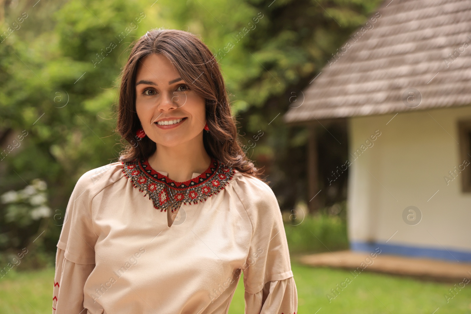 Photo of Beautiful woman wearing ornate beaded necklace in village, space for text. Ukrainian national jewelry