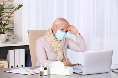 Photo of Ill mature woman with face mask suffering from cough at workplace