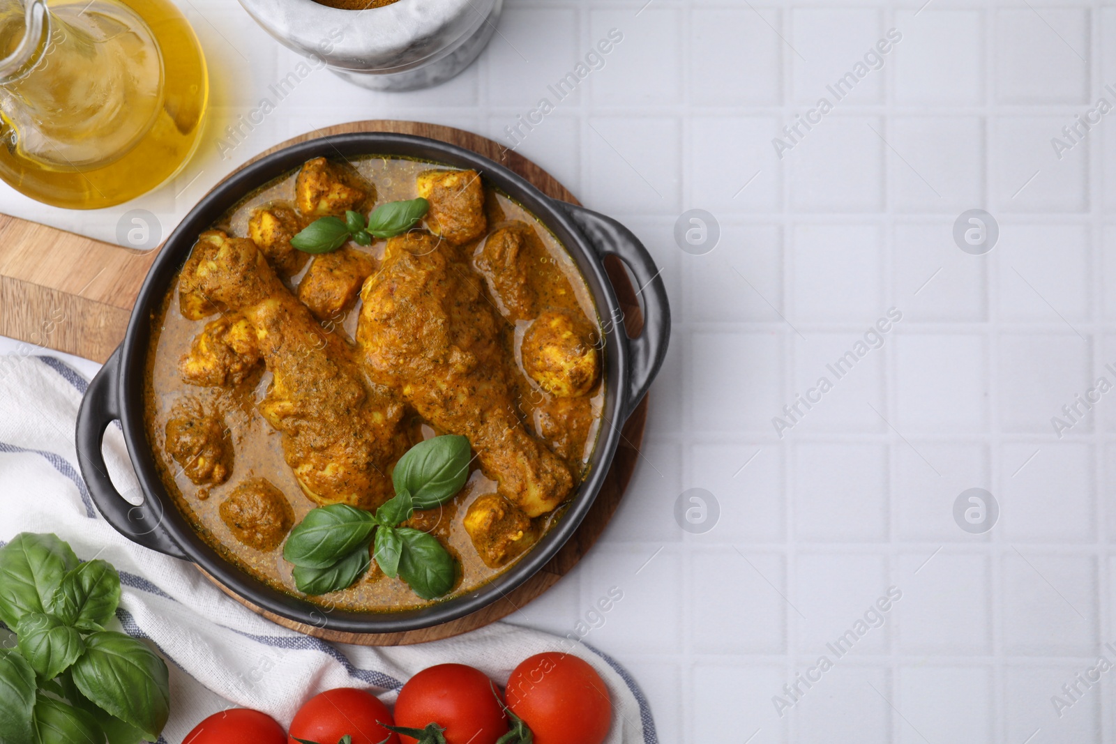 Photo of Delicious chicken with curry sauce and ingredients served on white tiled table, flat lay. Space for text