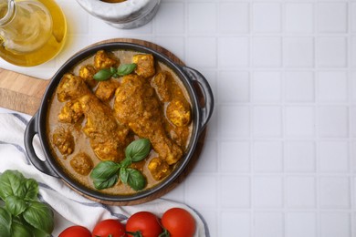 Delicious chicken with curry sauce and ingredients served on white tiled table, flat lay. Space for text