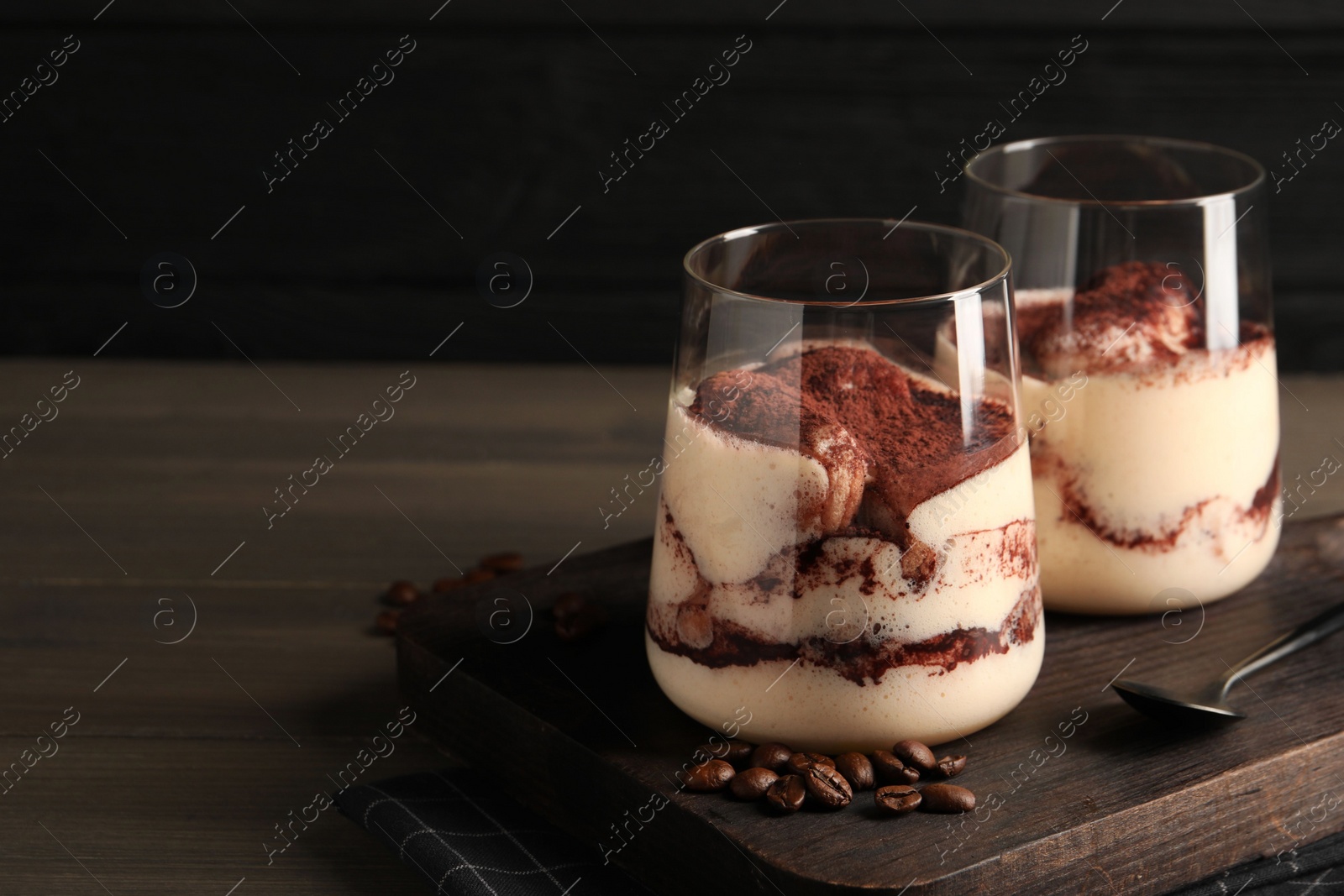 Photo of Delicious tiramisu in glasses, spoon and coffee beans on wooden table. Space for text