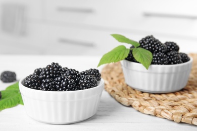 Bowls of tasty blackberries with leaves on white wooden table