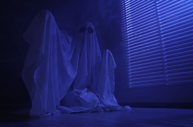 Photo of Creepy ghost. Woman covered with sheet near window in blue light, low angle view. Space for text