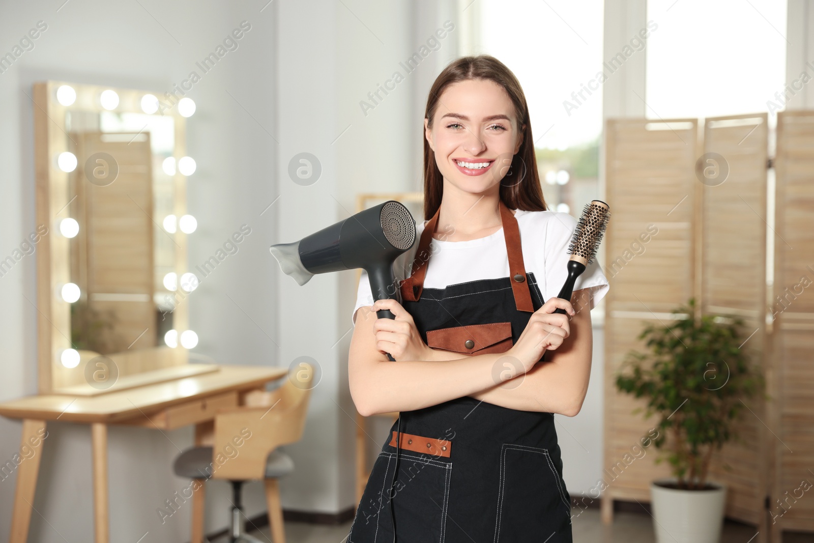 Photo of Portrait of happy hairdresser with hairdryer and brush in beauty salon