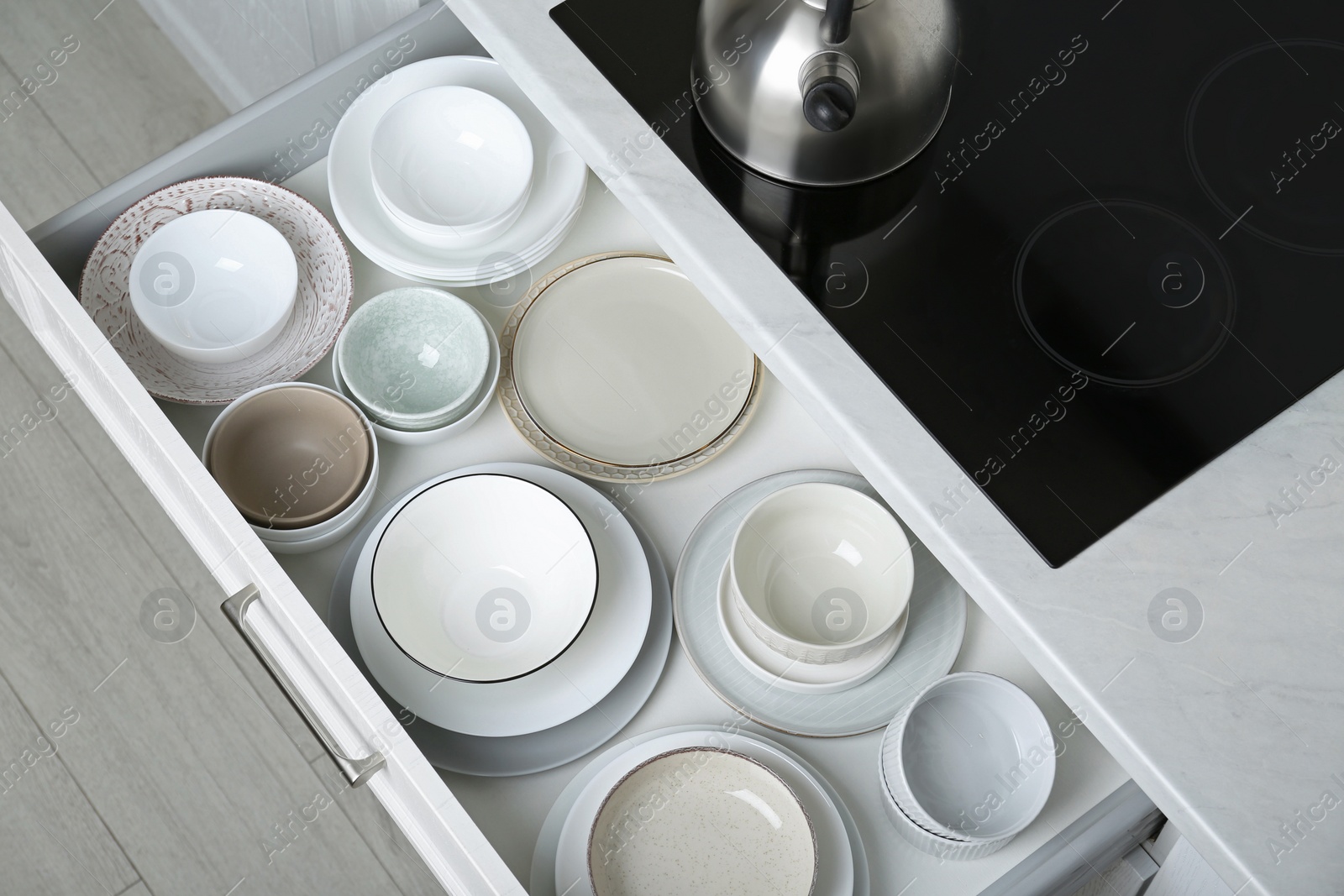 Photo of Open drawer with different plates and bowls in kitchen, above view