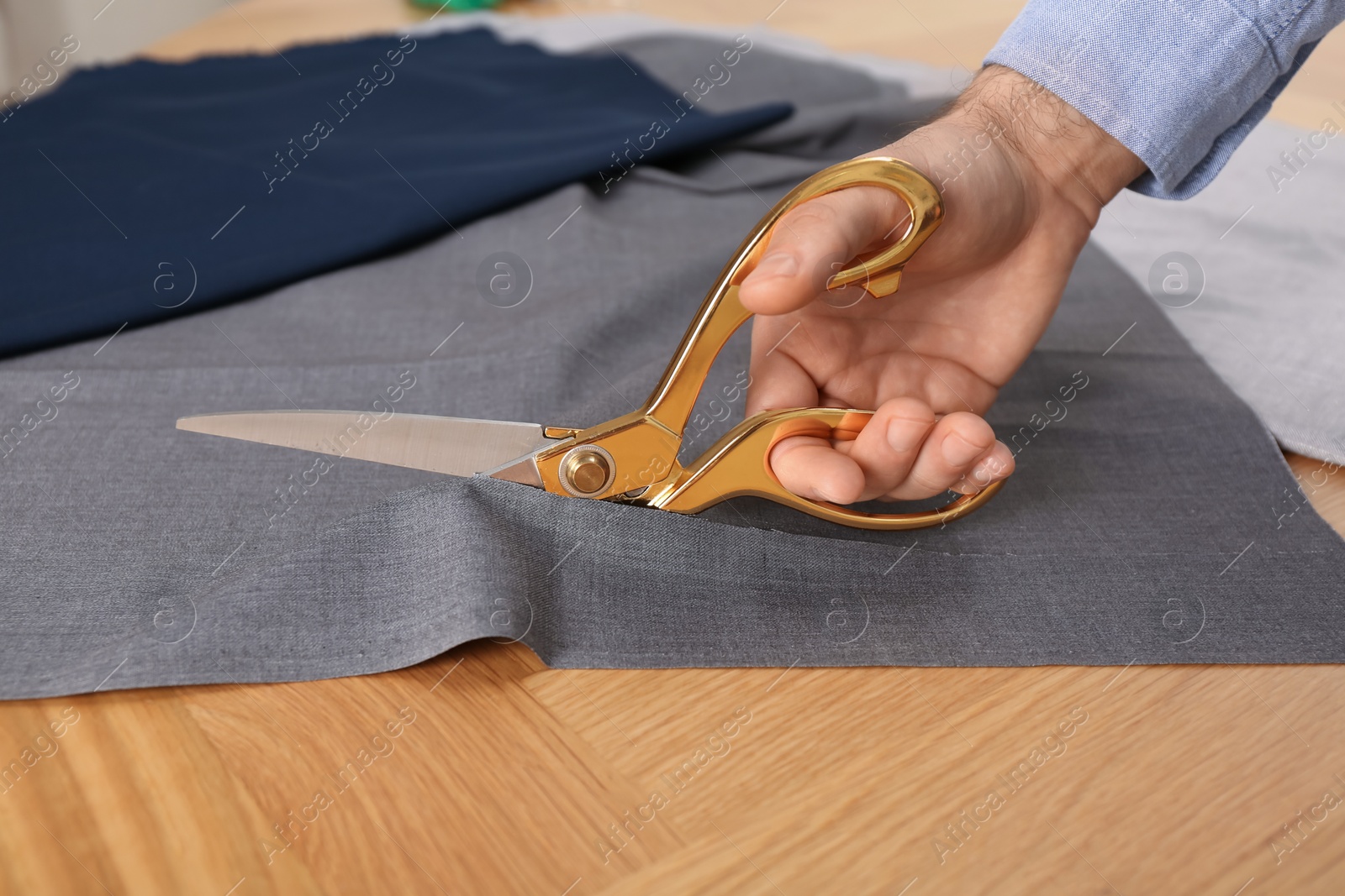 Photo of Man cutting grey fabric with scissors at wooden table, closeup