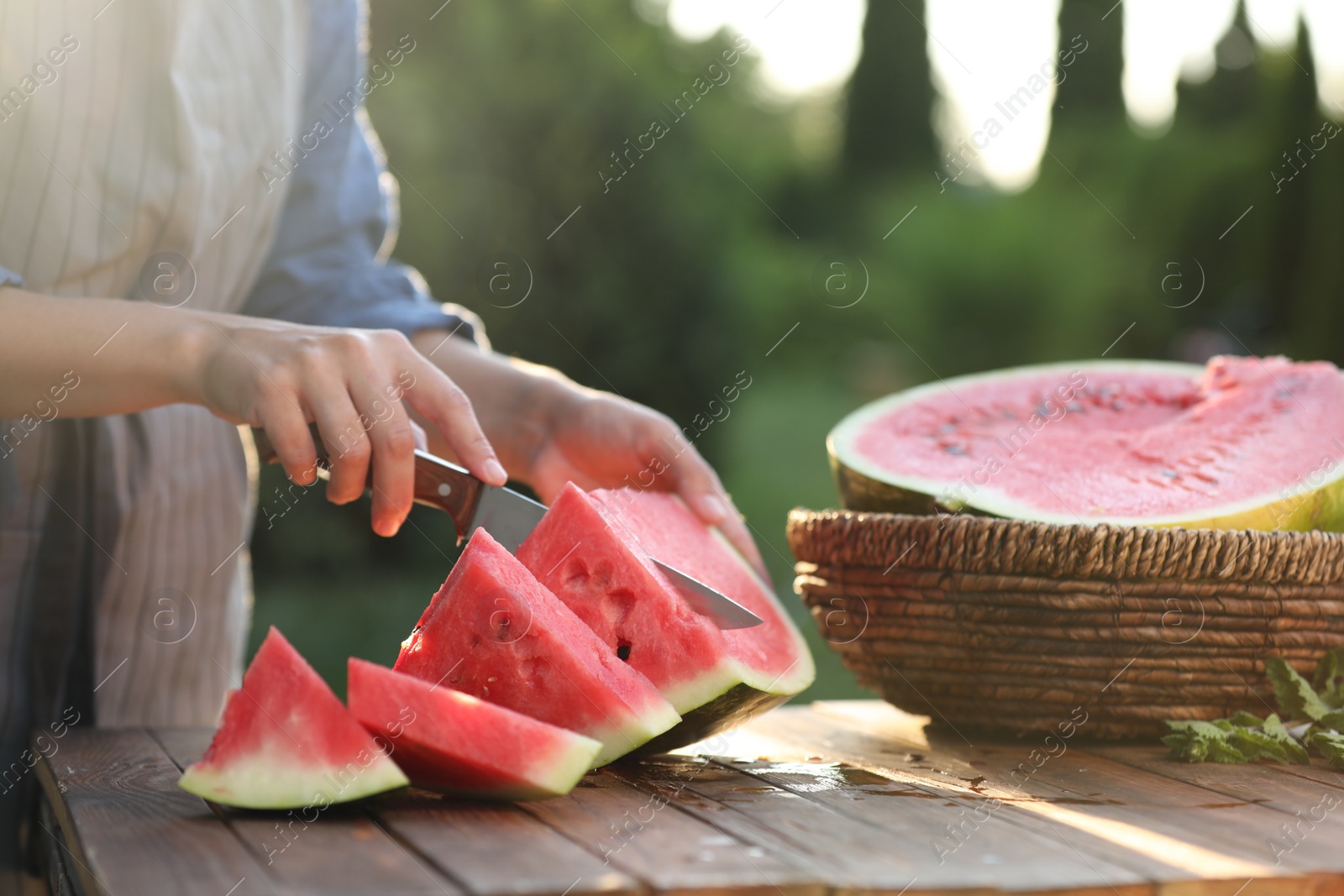 Photo of Woman cutting tasty ripe watermelon at wooden table outdoors, closeup