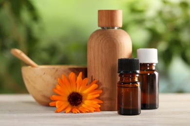 Photo of Bottles of essential oils and beautiful calendula flower on white wooden table outdoors, closeup