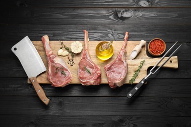 Photo of Fresh tomahawk beef cuts, spices and butcher tools on black wooden table, top view