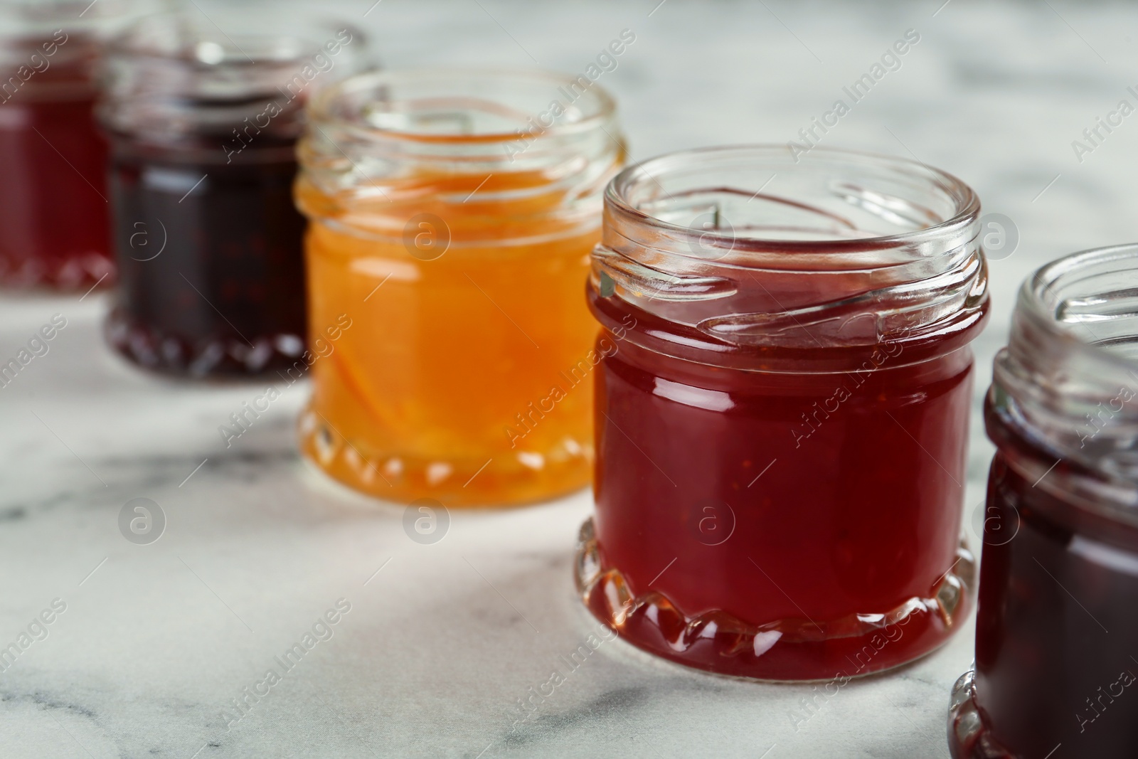 Photo of Jars of different jams on white marble table, closeup