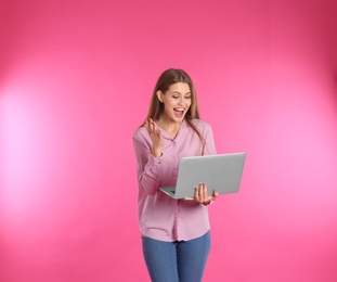 Photo of Emotional young woman with laptop celebrating victory on color background