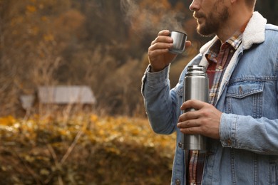 Man with metallic thermos and cup lid in nature, closeup. Space for text