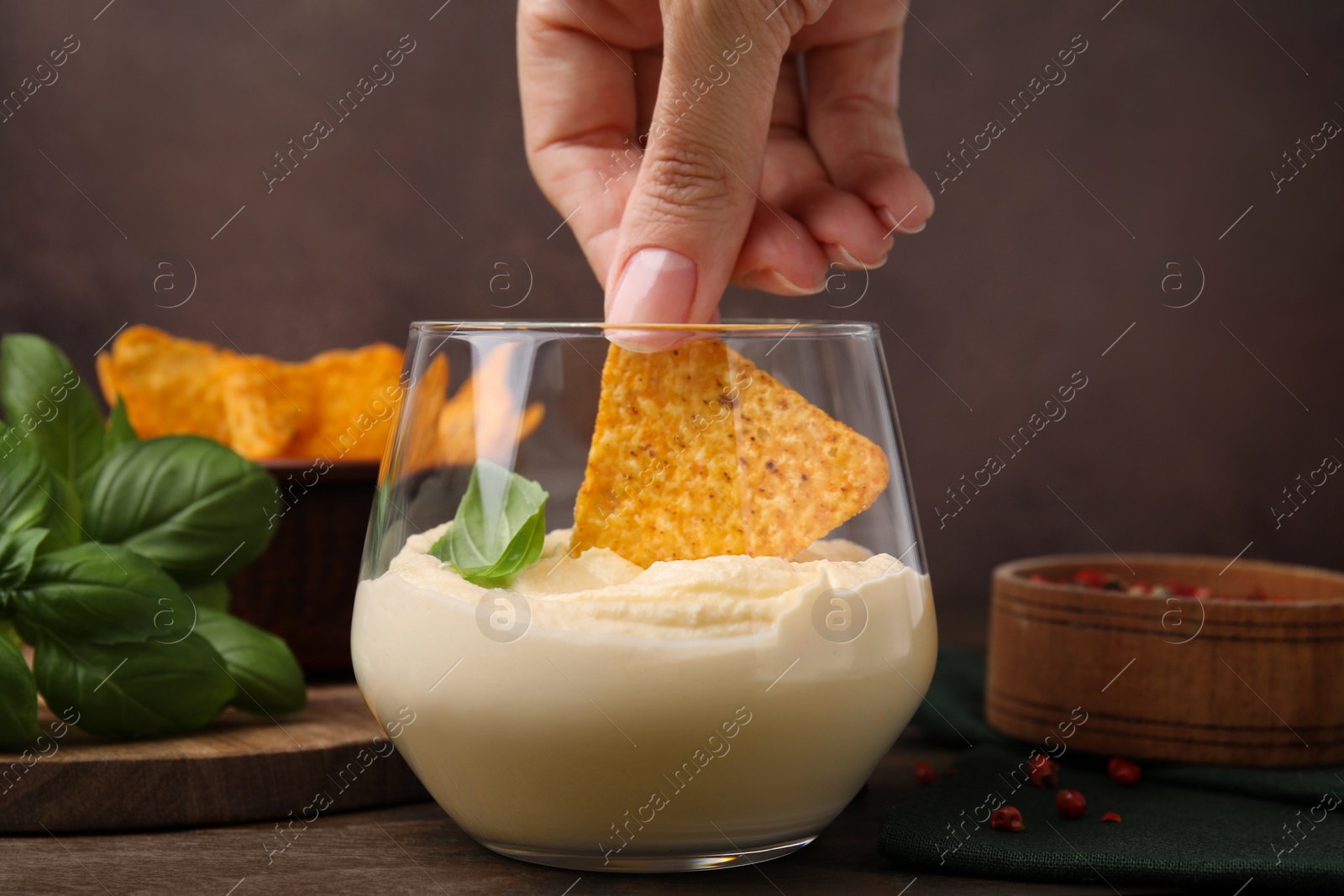 Photo of Woman dipping nachos chip into delicious tofu sauce at wooden table, closeup