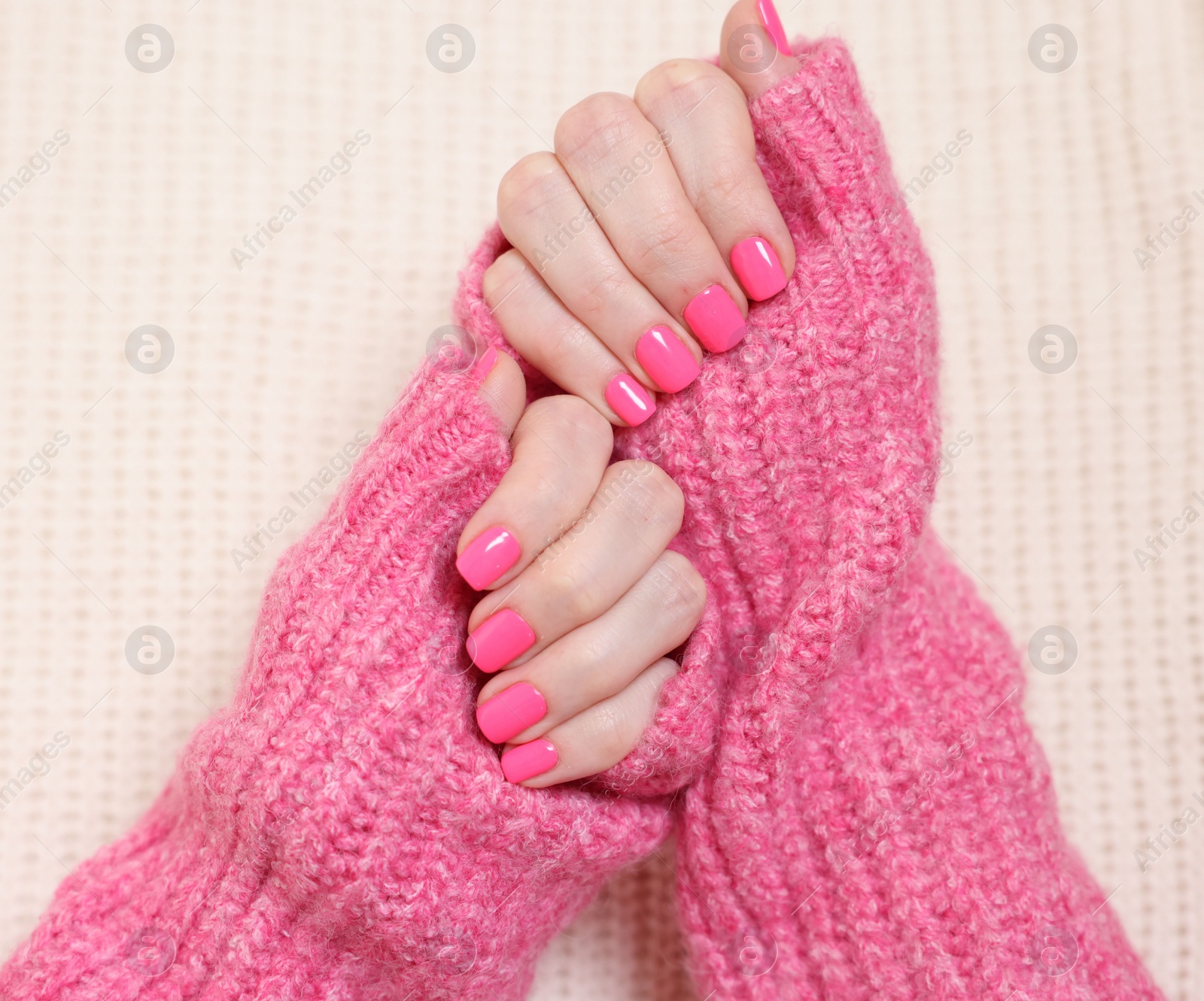 Photo of Woman showing her manicured hands with pink nail polish on knitted blanket, top view