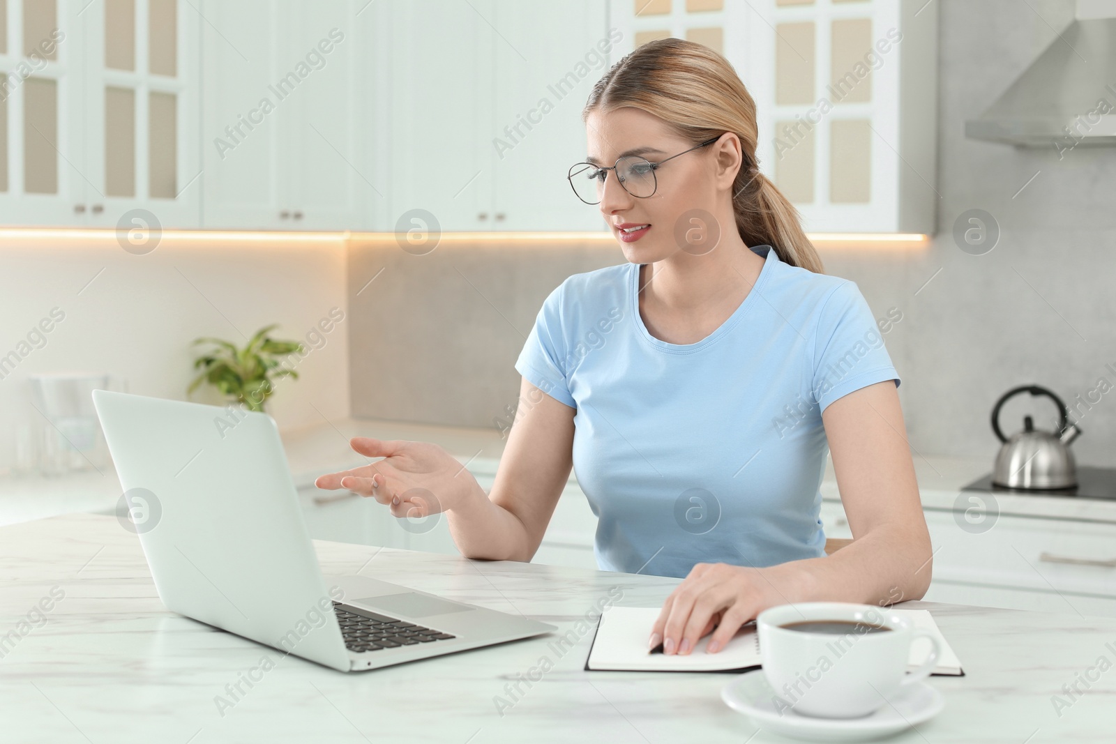 Photo of Home workplace. Woman talking by videochat on laptop at marble desk in kitchen