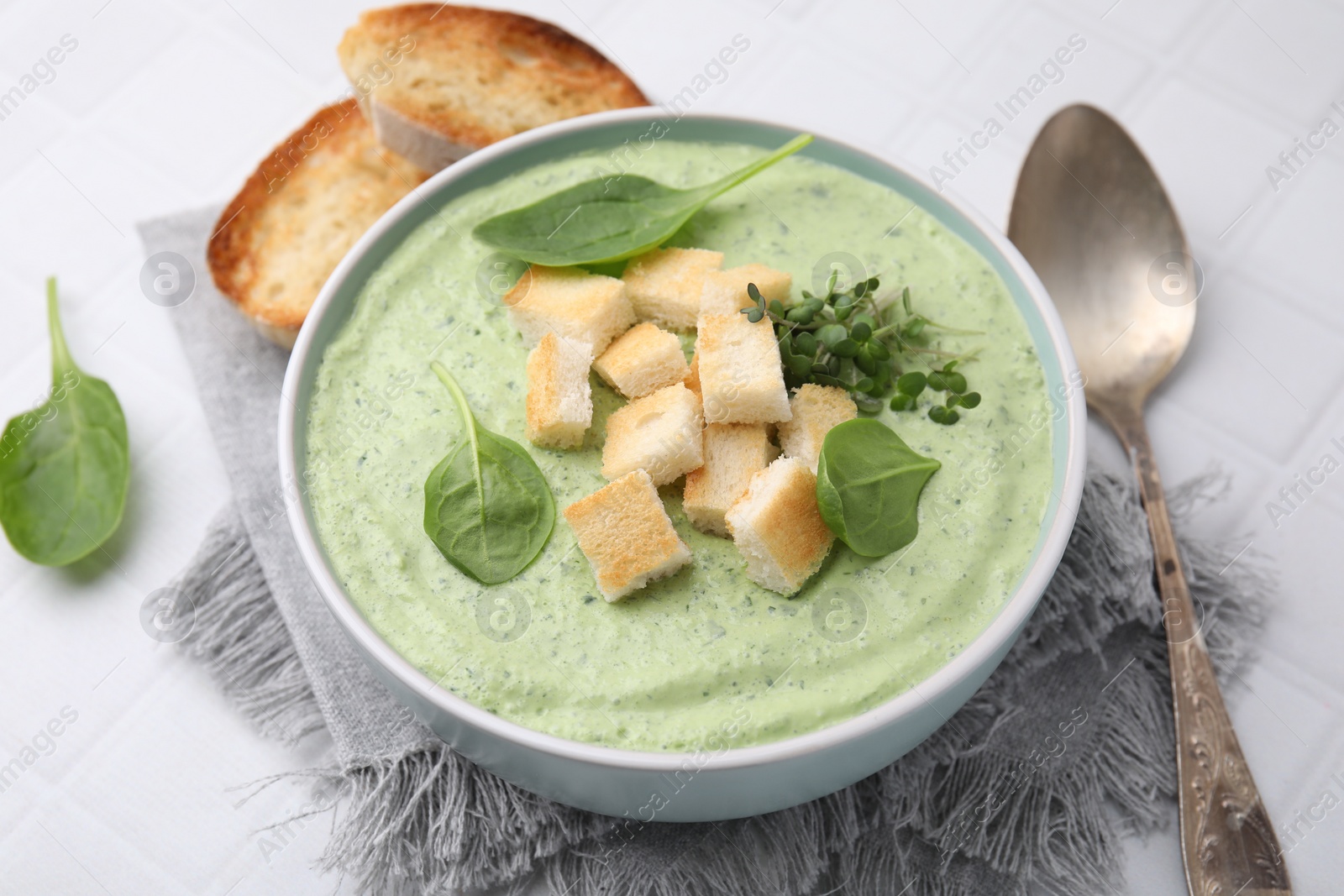 Photo of Delicious spinach cream soup with croutons in bowl on white tiled table