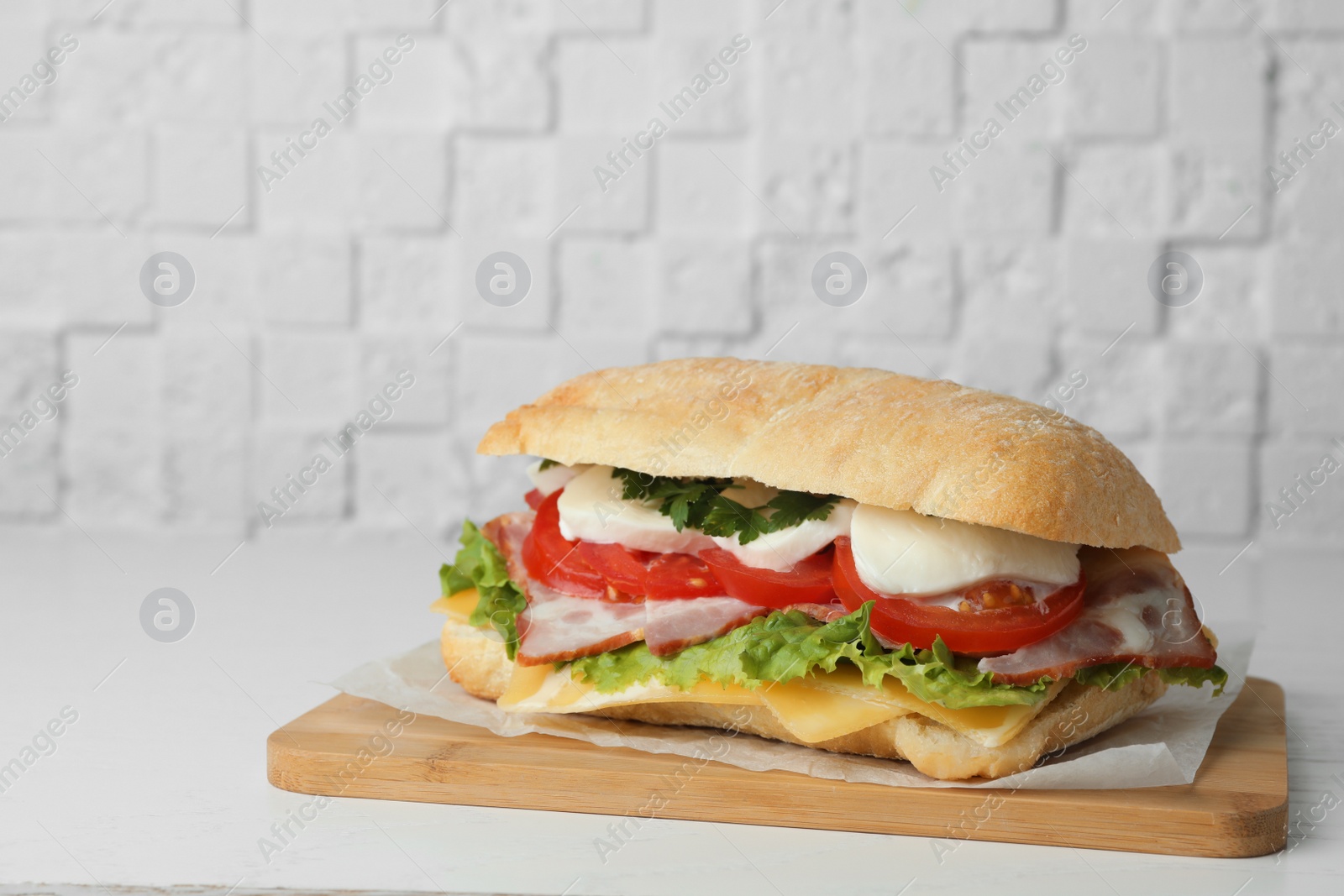 Photo of Delicious sandwich with fresh vegetables and mozzarella on white table