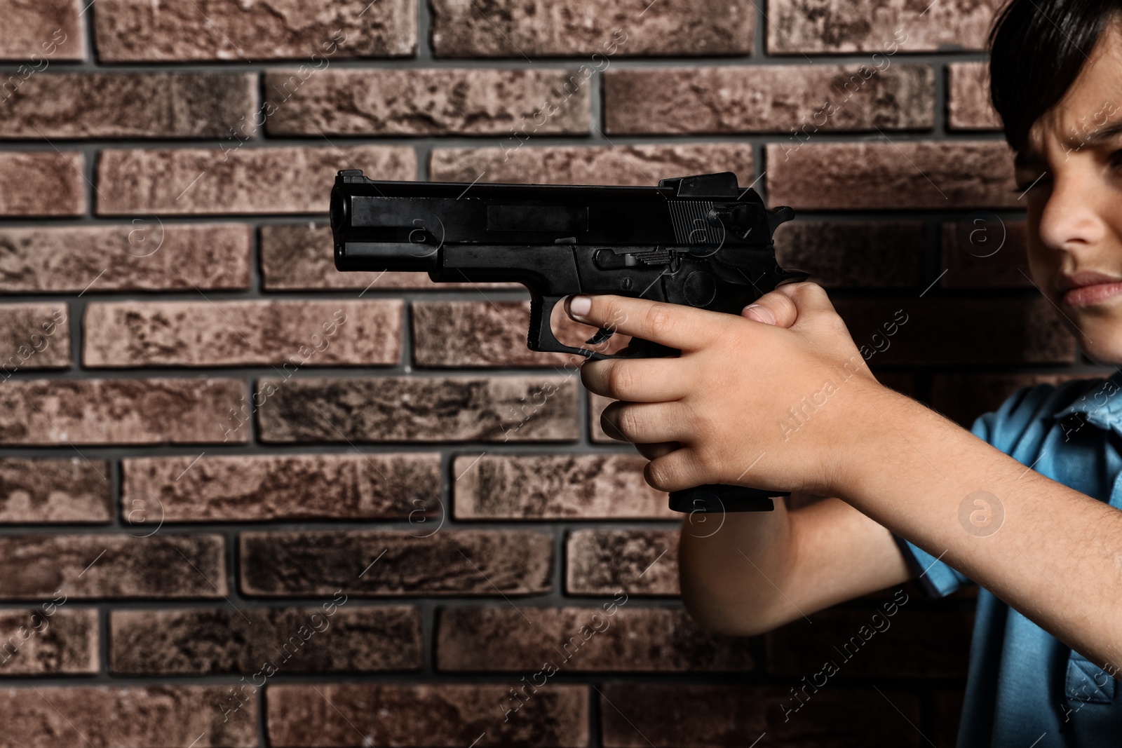 Photo of Little child playing with gun against brick wall. Dangerous game