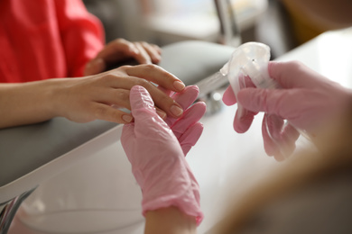 Photo of Professional manicurist applying antiseptic on client's hands in beauty salon, closeup