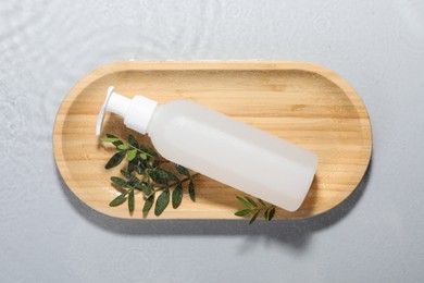 Photo of Wooden tray with bottle of facial cleanser and leaves on light grey background, top view