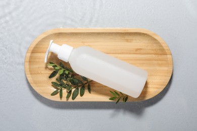 Wooden tray with bottle of facial cleanser and leaves on light grey background, top view