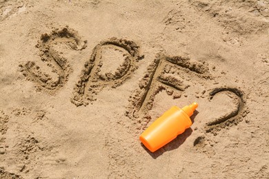 Photo of Abbreviation SPF and question mark written on sand, blank bottle of sunscreen at beach, above view