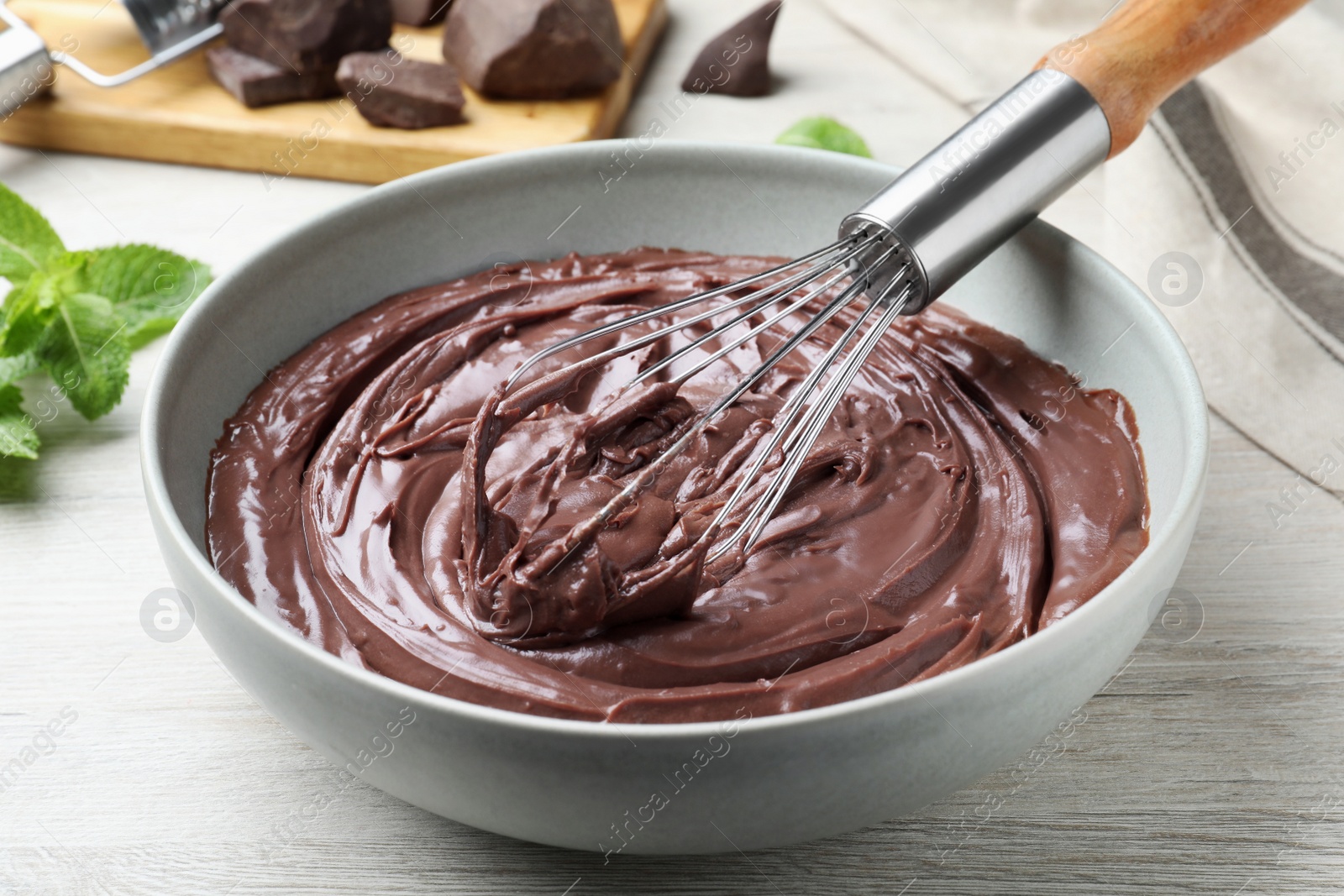 Photo of Whipping chocolate cream with balloon whisk on white wooden table, closeup