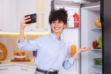 Smiling food blogger taking selfie near fridge in kitchen
