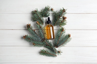 Little bottle with essential oil and pine branches on wooden background, flat lay