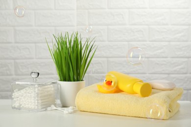 Photo of Baby bath accessories. Towel, cosmetic products, cotton swabs and toy duck on white table against brick wall