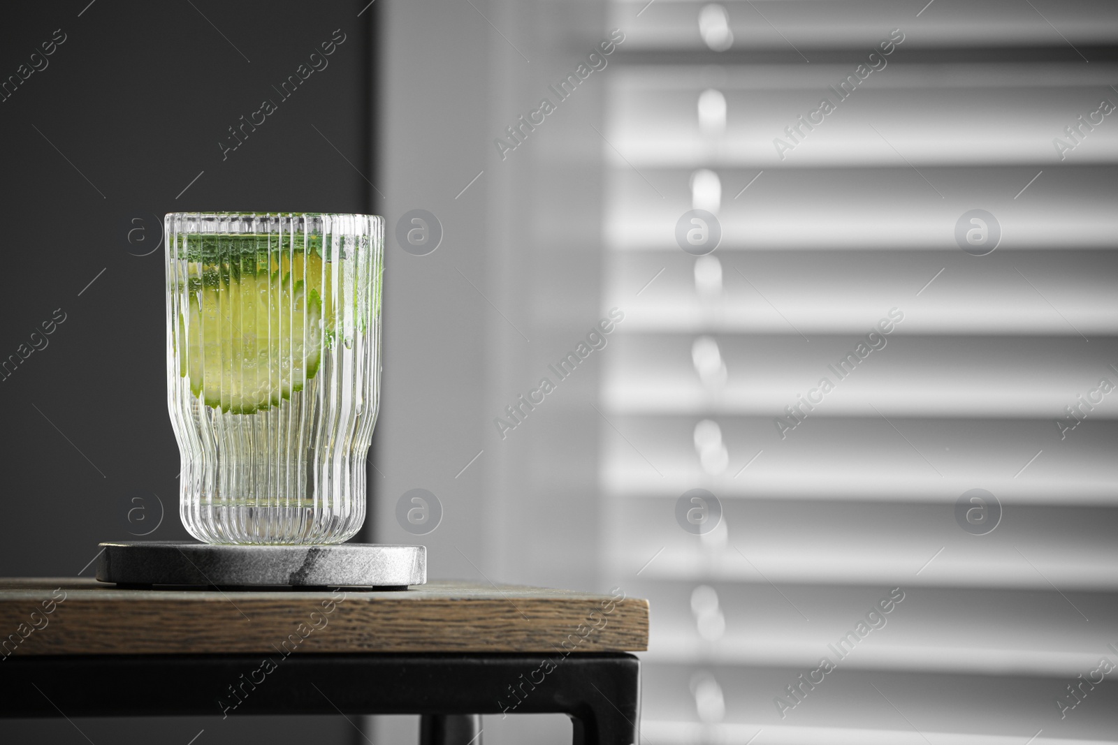 Photo of Glass of lemonade and stylish cup coaster on wooden table in room. Space for text