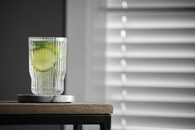 Glass of lemonade and stylish cup coaster on wooden table in room. Space for text