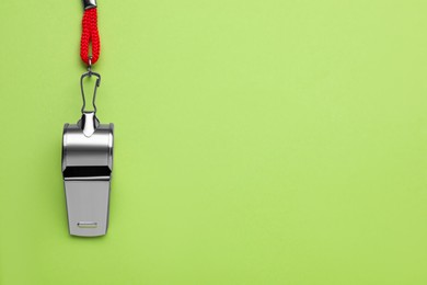 One metal whistle with red cord on light green background, top view. Space for text