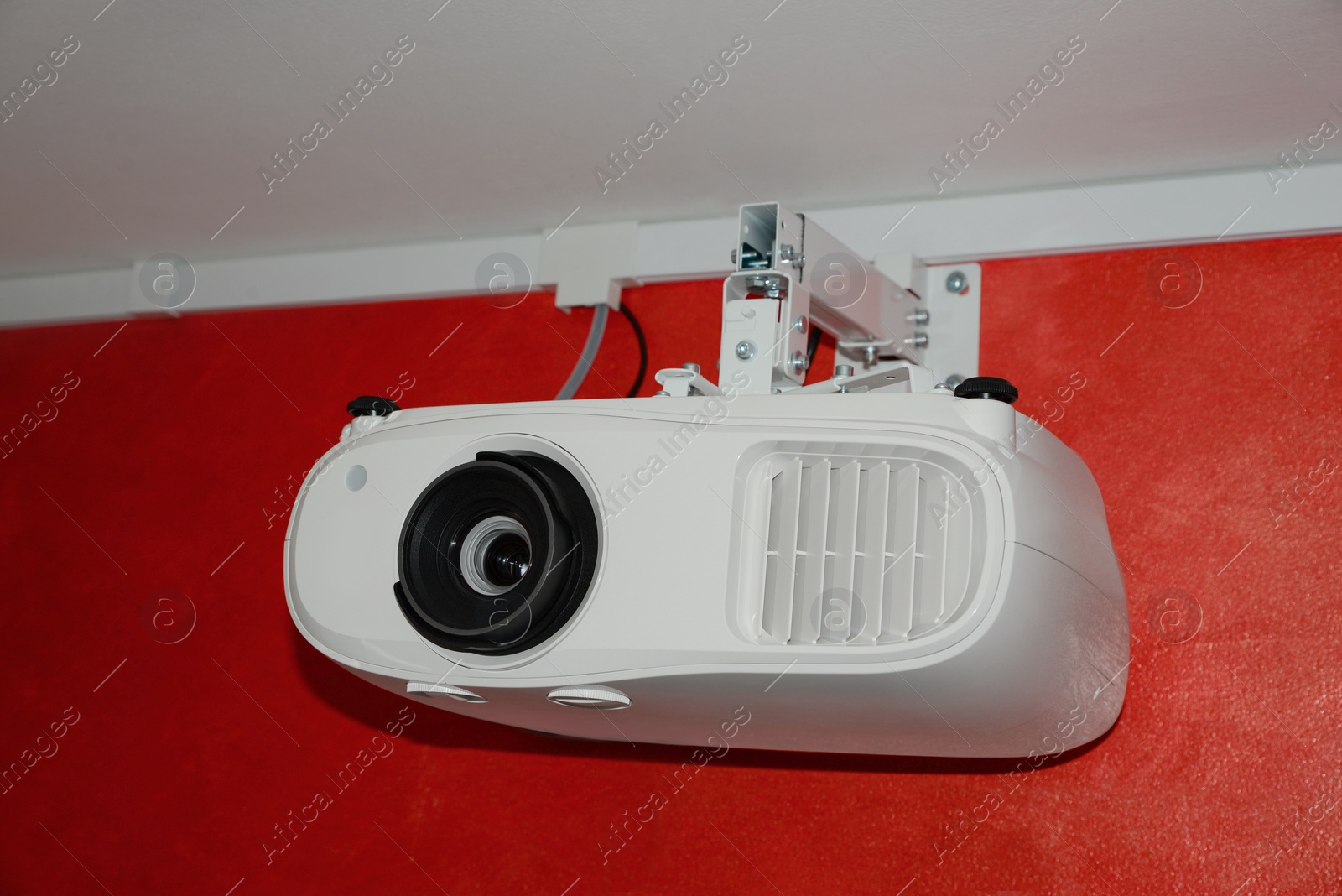 Photo of Modern digital video projector on red wall indoors