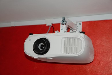 Photo of Modern digital video projector on red wall indoors
