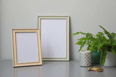 Photo of Empty photo frames, candles and green plant on grey table