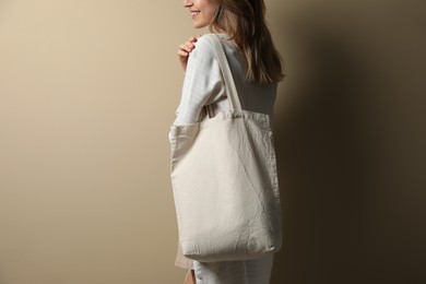 Photo of Happy young woman with blank eco friendly bag against beige background, closeup