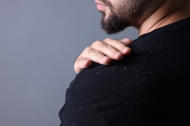 Photo of Man brushing dandruff off his sweater on grey background, closeup. Space for text