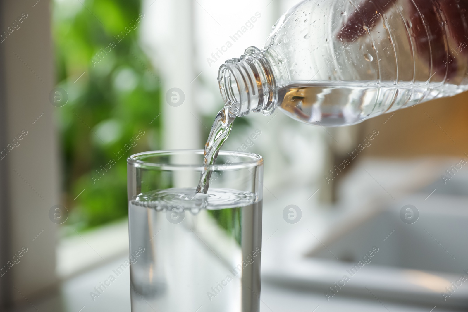 Photo of Person pouring water from bottle into glass in kitchen, closeup