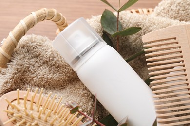 Photo of Dry shampoo spray, towel and hairbrushes with eucalyptus branch in basket on table, closeup