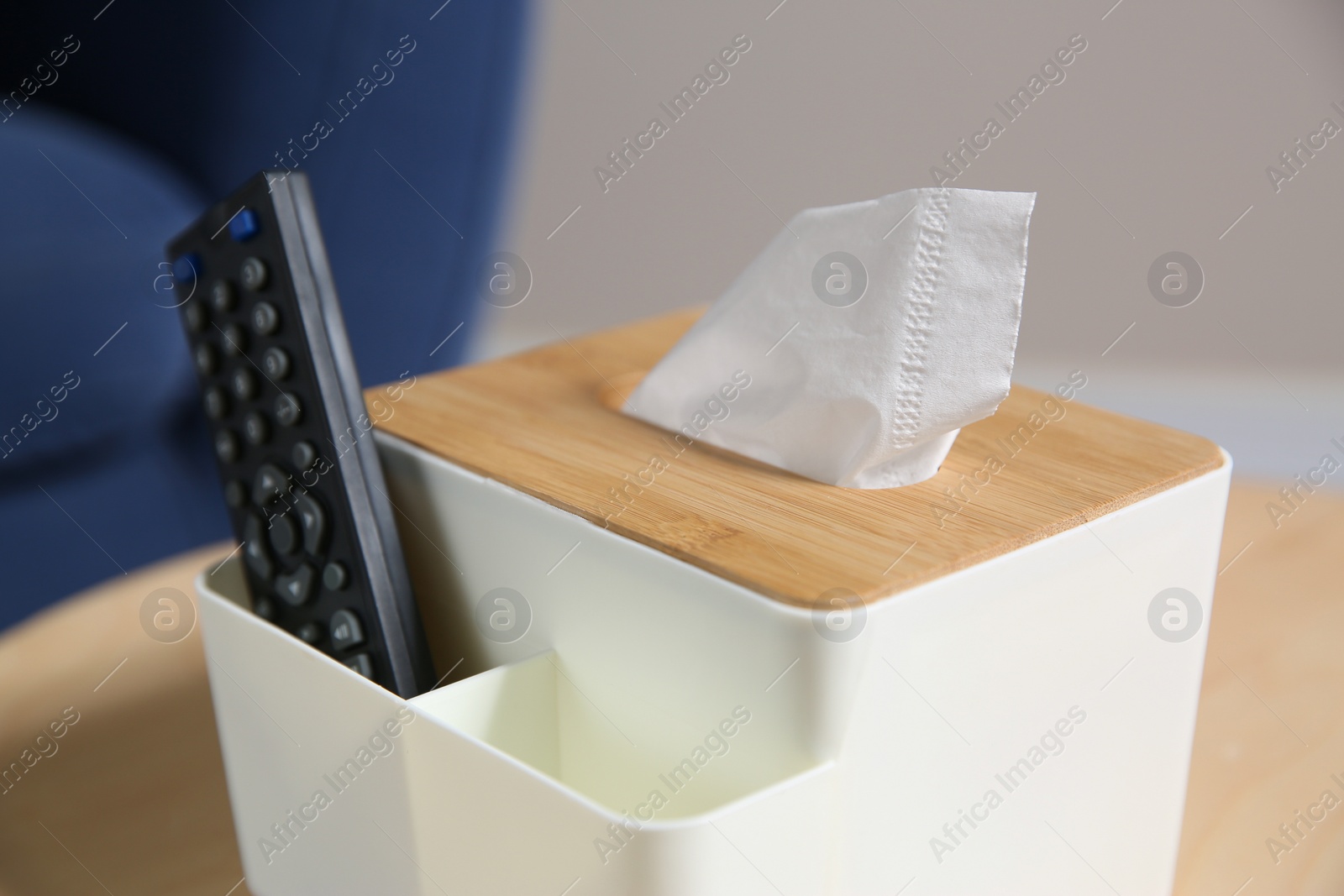 Photo of Box with paper tissues and TV remote control on wooden table in living room, closeup