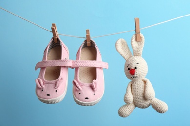 Photo of Small shoes and toy bunny hanging on washing line against color background. Baby accessories