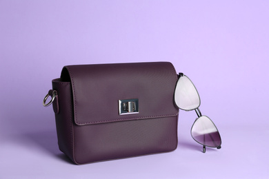 Stylish woman's bag and sunglasses on lilac background