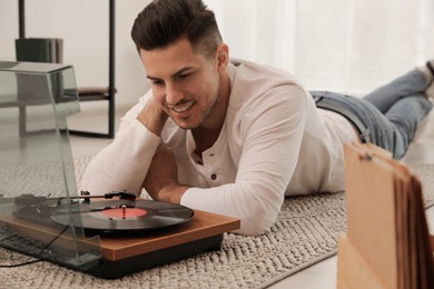 Photo of Happy man listening to music with turntable while lying on floor at home